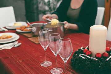 Foreground focus on empty wine glasses, with woman serving food on Christmas table in background