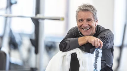Foto op Aluminium Fit in his sixties, man rests on a towel smiling inside the gym © weyo