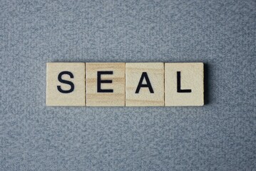 text the word seal from brown wooden small letters with black font on an gray table