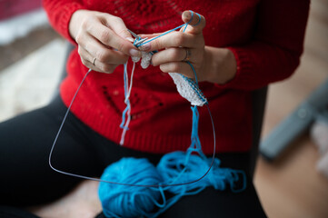 Woman in red sweater knitting with blue cotton thread