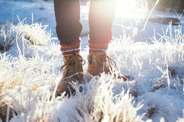 Front view on winter warm heavy duty leather boots or hiking shoes stand in frosty snow with sun flare. Cosy winter hike, with warm handmade knit wool socks with traditional ornament 