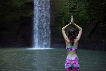 Hands raising up in namaste mudra. Woman meditating, practicing yoga and pranayama with namaste mudra near waterfall. Yoga outdoor concept. Tibumana waterfall, Bali. Copy space. View from back.
