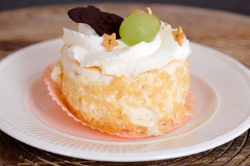 Pastry with whipped cream, chocolate, white raisin on a porcelain plate on a wooden table.