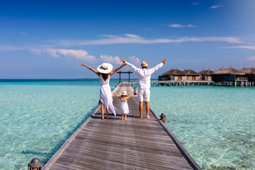 A happy family in white summer clothing on vacation walks along a wooden pier over tropical,...