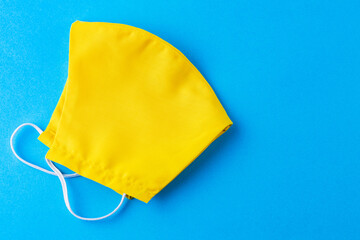 Reusable face mask made from yellow cotton. Face protective mask. Yellow protective mask on a blue background. Pop art style. Top view. Copy space