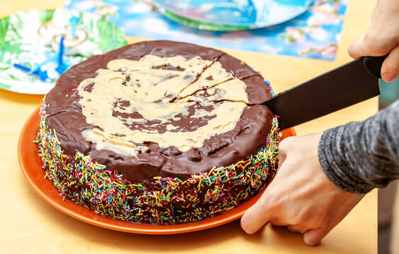 Person Cutting, Dividing A Homemade Chocolate Cake Decorated With Many Sprinkles Using A Knife, Hand Closeup. Home Made Cocoa Pastry, Birthday Cake Being Cut Up Close, From Above. Sharing Cake Concept