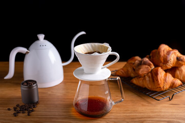 Drip brewing, filtered coffee or pour-over with croissants on wooden table. Breakfast concept.