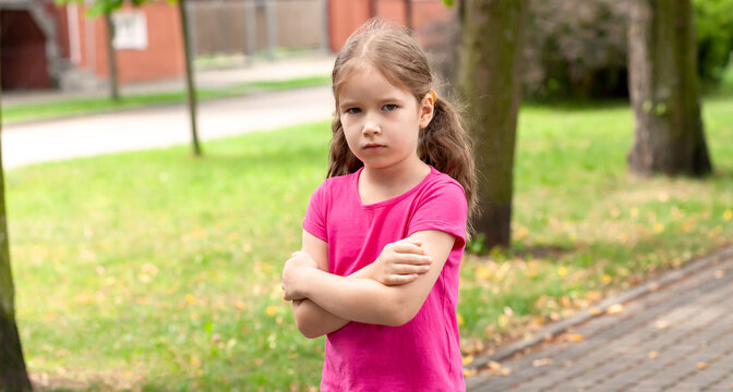 One lone offended child, sad anxious angry lone little girl standing slightly upset, kid with arms crossed, closeup, portrait, outdoors, copy space. Children and frustration, irritation, sadness - Powered by Adobe