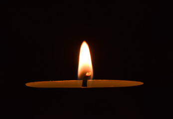 Jasny, mały płomień świeczki na ciemnym tle.
