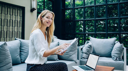 Portrait of cheerful pretty blonde businesswoman checking report satisfied with income using technology, positive female in elegant wear sitting at cafe terrace with laptop computer for job