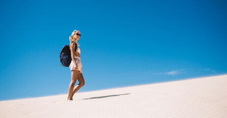 Caucasian female explorer with touristic backpack discovering wild nature sandy environment during summer vacations for recreate, young wanderer standing at Sahara horizon with dunes landscape © BullRun
