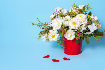 flowers for interior decoration in a red pot on a blue background, next to a confetti of red hearts