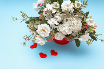 flowers for interior decoration in a red pot on a blue background, next to a confetti of red hearts