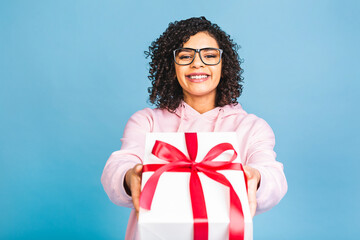 Fototapeta premium Happy african american curly lady in casual laughing while holding present gift box isolated over blue background.