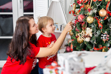 The New year holiday. Mom and child near the Christmas tree with decorations and gifts
