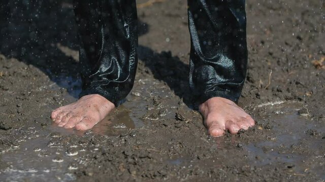 The Wanderer rejoices in the long-awaited rain in the desert. Male bare feet in black pants stand on wet ground, raindrops dripping on top of them. 200 fps slow motion