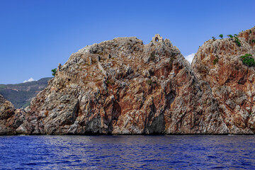 Fototapeta na wymiar Conical stone rock with ruins of ancient buildings in the middle of the blue waters of the Mediterranean Sea in Alanya (Turkey). Remains of the ancient walls of Alanya Castle on the steep slope