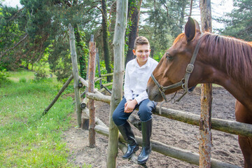 In summer, on a bright sunny day, a boy is sitting next to a horse on a ranch. - Powered by Adobe