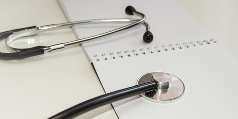 Stethoscope lies on an open empty notebook close-up at the workplace of a family doctor, a medical examination is carried out, the concept of medical care
