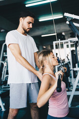 Fototapeta premium Cheerful young woman wearing pink sports bra while doing chin-up exercise with trainer man