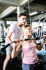 Fototapeta na wymiar Cheerful young woman wearing pink sports bra while doing chin-up exercise with trainer man