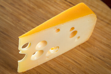 Yellow cow's milk Swiss cheese emmenthal with holes on wooden board..
