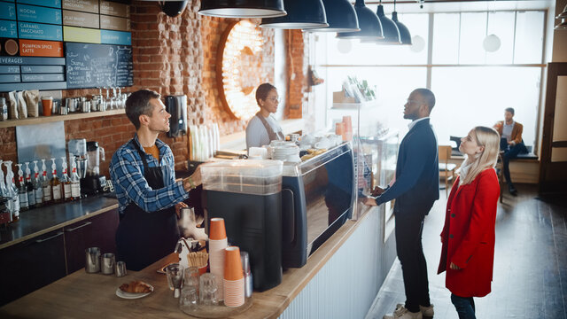 Latin Female Cashier and Male Barista in Checkered Shirt Accept Orders from Diverse Clients in Coffee Shop Bar. African American Handsome Customer Orders Take Away Latte from a Cozy Lifestyle Cafe.