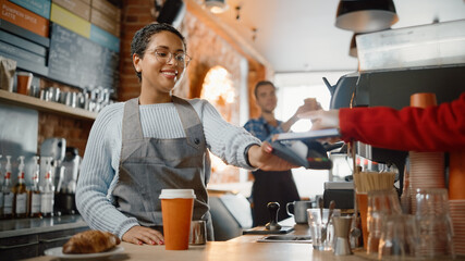 Joyful Multiethnic Diverse Woman Gives a Payment Terminal to Customer Using NFC Technology on Smartphone. Customer Uses Mobile to Pay for Take Away Latte and Croissant to a Barista in Coffee Shop.