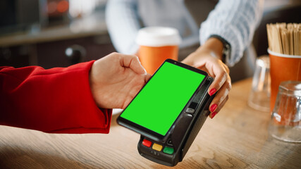 Close Up of a Feminine Hand Holding a Smartphone with Green Screen Template with an NFC Payment Technology Used for Paying for Take Away Coffee in a Cafe. Customer Uses Mobile to Pay for Latte