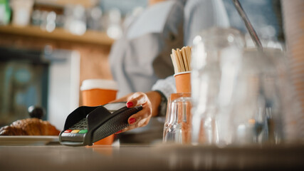 Close Up of a Feminine Hand Holding a Smartphone with an NFC Payment Technology Used for Paying for Take Away Coffee in a Cafe. Customer Uses Mobile to Pay for Latte Through a Credit Card Terminal.