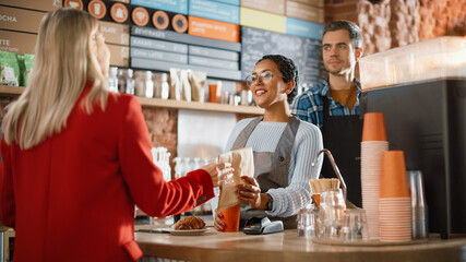 Joyful Multiethnic Diverse Woman Gives a Payment Terminal to Customer Using NFC Technology on Smartphone. Customer Uses Mobile to Pay for Take Away Latte and Pastry to a Barista in Coffee Shop.