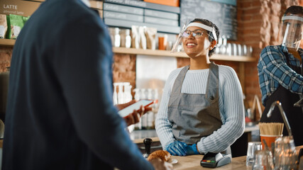 Male Customer Pays for Coffee and Pastry with Contactless NFC Payment Technology on Smartphone to a Barista in Face Shield in Cafe. Social Restrictions Concept in a Bar During Coronavirus Pandemic.