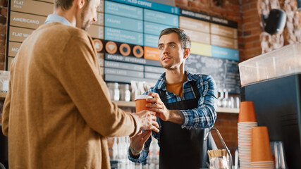 Tall Caucasian Customer in Yellow Shirt Pays and Takes Take Away Cardboard Cup of Coffee from a Handsome Barista in Blue Checkered Shirt. Contactless Mobile Payment in Cafe Concept.