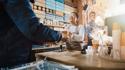 Black African American Food Delivery Courier Picking Up Two Take Away Coffees and Pastries from a Cafe Restaurant. Happy Diverse Staff Give the Order and Put it in a Hot Thermal Insulated Bag.