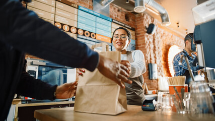 Beautiful Happy Latin Barista Serves Order to a Food Delivery Courier Picking Up Paper Bag with Pastries from a Cafe Restaurant. Delivery Guy Puts Food in His Hot Thermal Insulated Bag. - Powered by Adobe