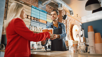 Shot in Modern Hipster Cafe: Handsome Smiling Barista in Checkered Shirt Passes Cardboard Cupholder with Two Take Away Coffee Cups to a Young Female Customer in Red Coat. Sunny Day with Happy People.