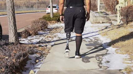 Afircan-American man artificial prosthetic leg walks down sidewalk