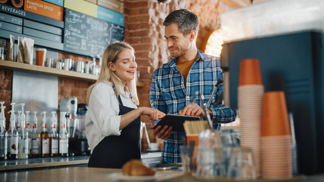 Two Diverse Entrepreneurs Have a Team Meeting in Their Stylish Coffee Shop. Barista and Cafe Owner Discuss Work Schedule and Menu on Tablet Computer. Young Female and Male Restaurant Employees.