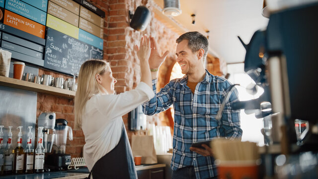 Two Diverse Entrepreneurs Have a Team Meeting in Their Stylish Coffee Shop. Barista and Cafe Owner Discuss Work Schedule and Menu on Tablet Computer. Young Female and Male Give Each Other High Five.