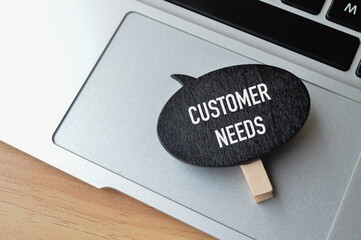 Top view of laptop and wooden board written with text CUSTOMER NEEDS. Business concept. 