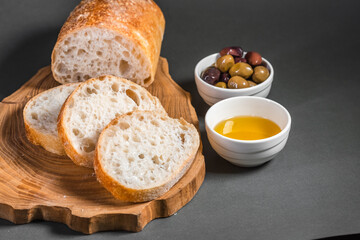 Traditional Italian ciabatta with olives and olive oil on a wooden board on the table. Craft bread and healthy food concept