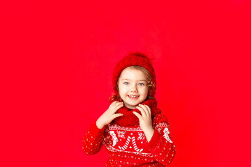 Obraz na płótnie Canvas a little girl in winter clothes rejoices on a red background. New year's concept