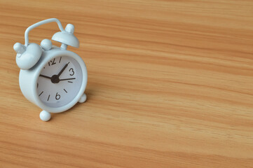 Top angle view of white clock over wooden background. Copy space for the text.