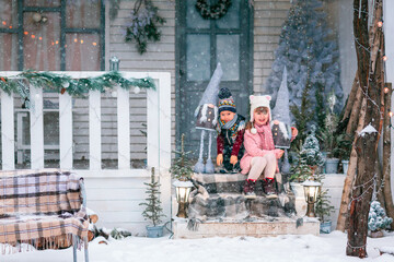 Happy little kids sitting on the porch of the Christmas decorated house outdoor
