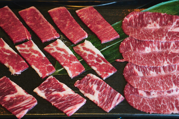 Top view. Assorted raw wagyu beef on a black dish with a green leaf.