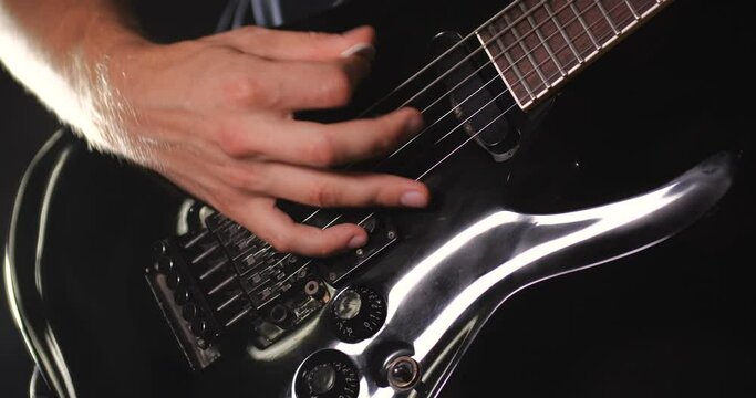 Unrecognizable rock musician in black clothes plays black electric guitar on black background isolated and smoke. Close up of hand and soundboard