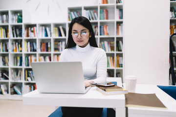 Attentive adult ethnic woman working at laptop in library