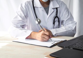 Doctor writing document at desk in clinic working on computer at room office.