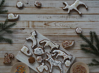 Homemade Christmas cookies in the shape of animals are laid out on a wooden background with fir branches. Christmas decor.