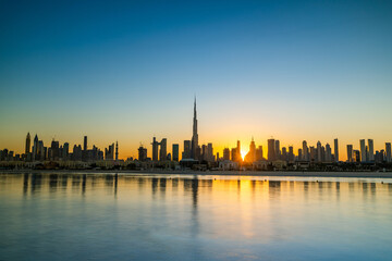 Fototapeta na wymiar Sunrise in Dubai with clean blue sky view from boat or sea. The Sun rises over UAE skyscrapers at morning. Dubai beach, coast, shore